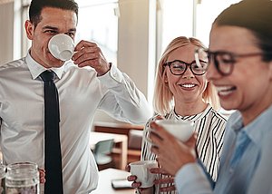 Ein Mann und zwei Frauen lachen und trinken Kaffee